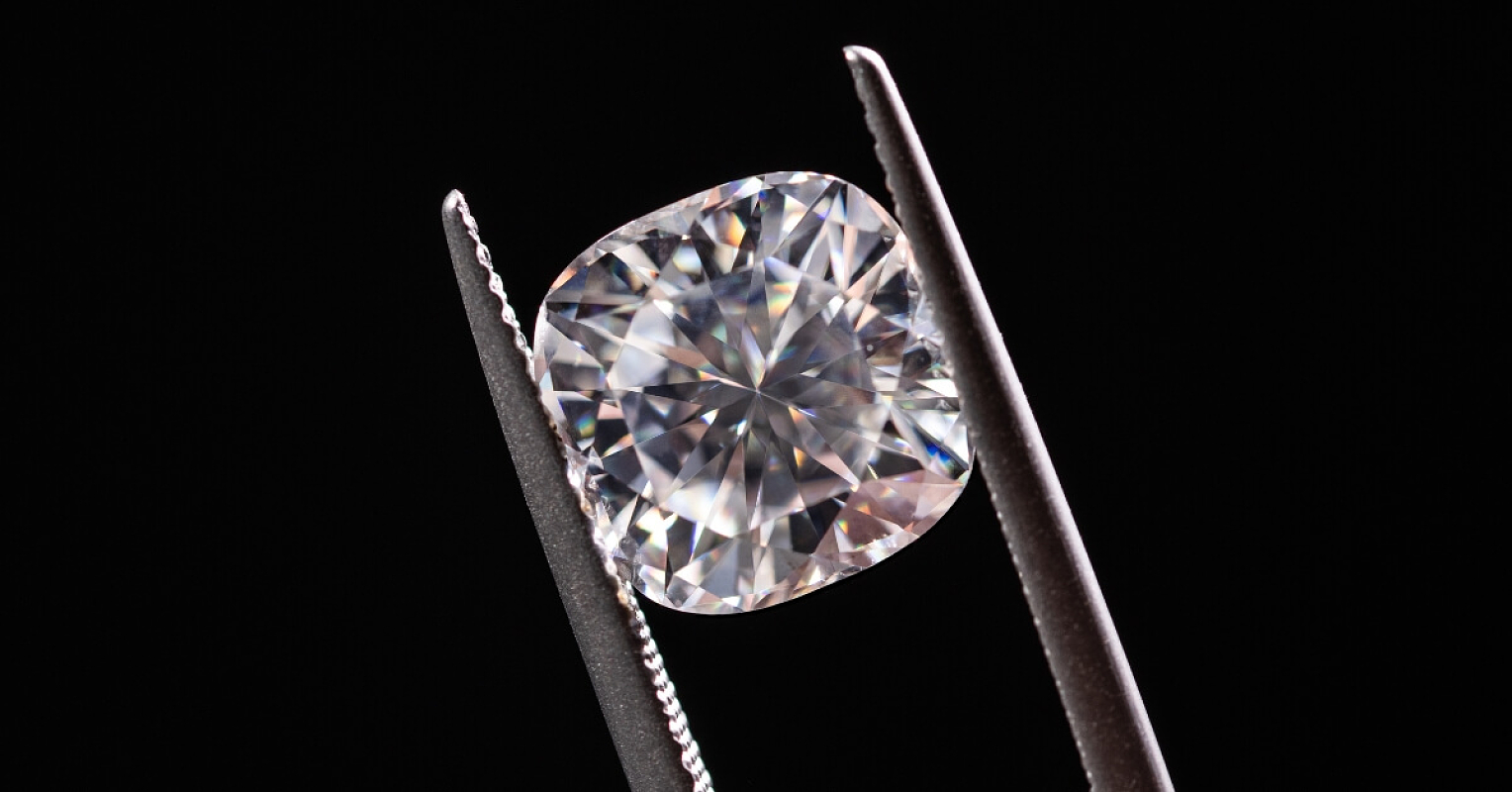 a moissanite in between a metal, silver tweezer in isolated dark background
